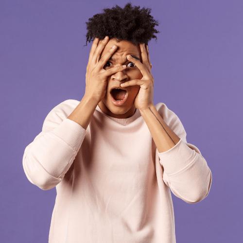 Young man against purple background, holding his hands to his face with a shocked expression