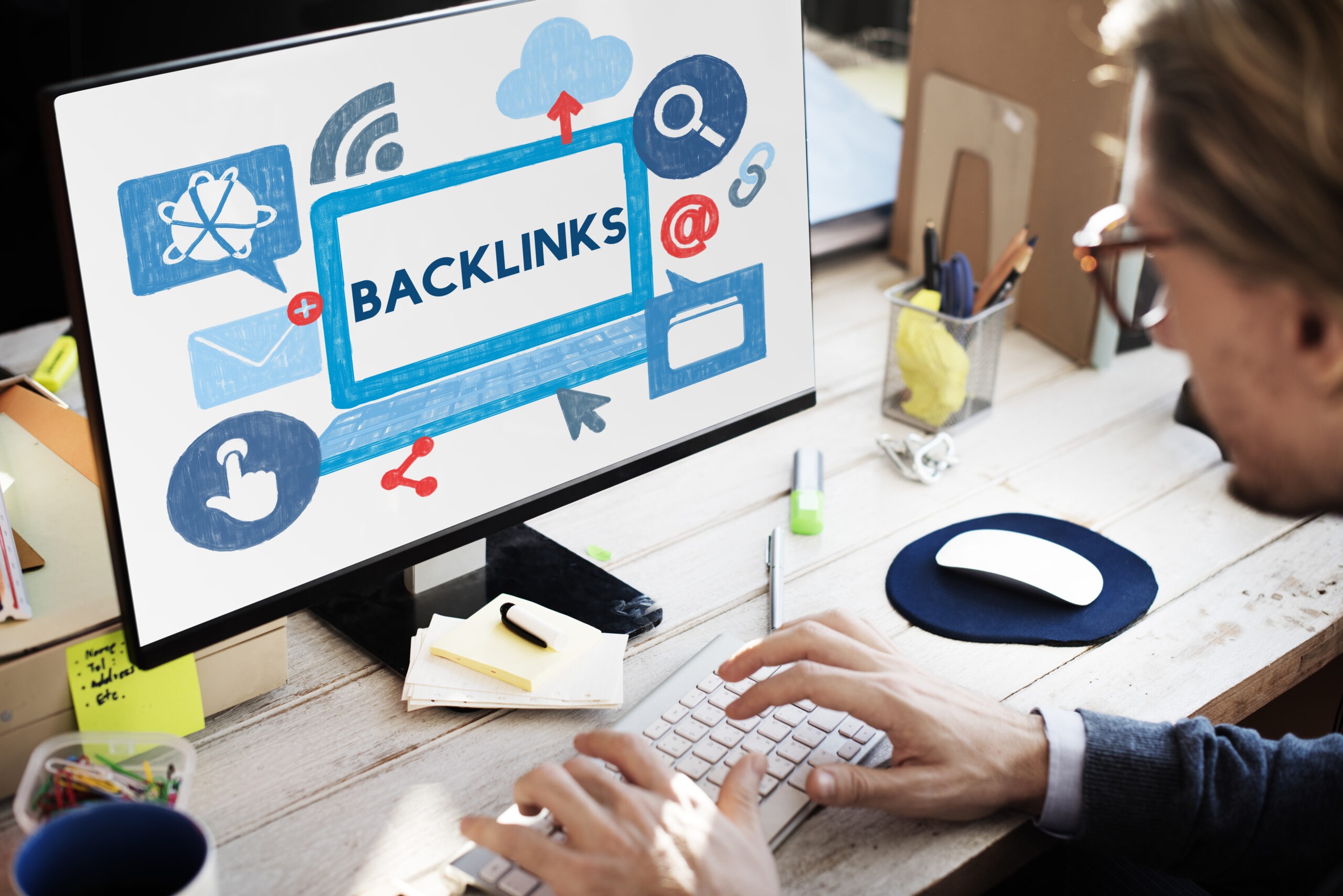 A person sitting in front of a computer. They are typing while the screen a displaying a graphic and in the middle of graphic the word, "Backlinks" is displayed. 
