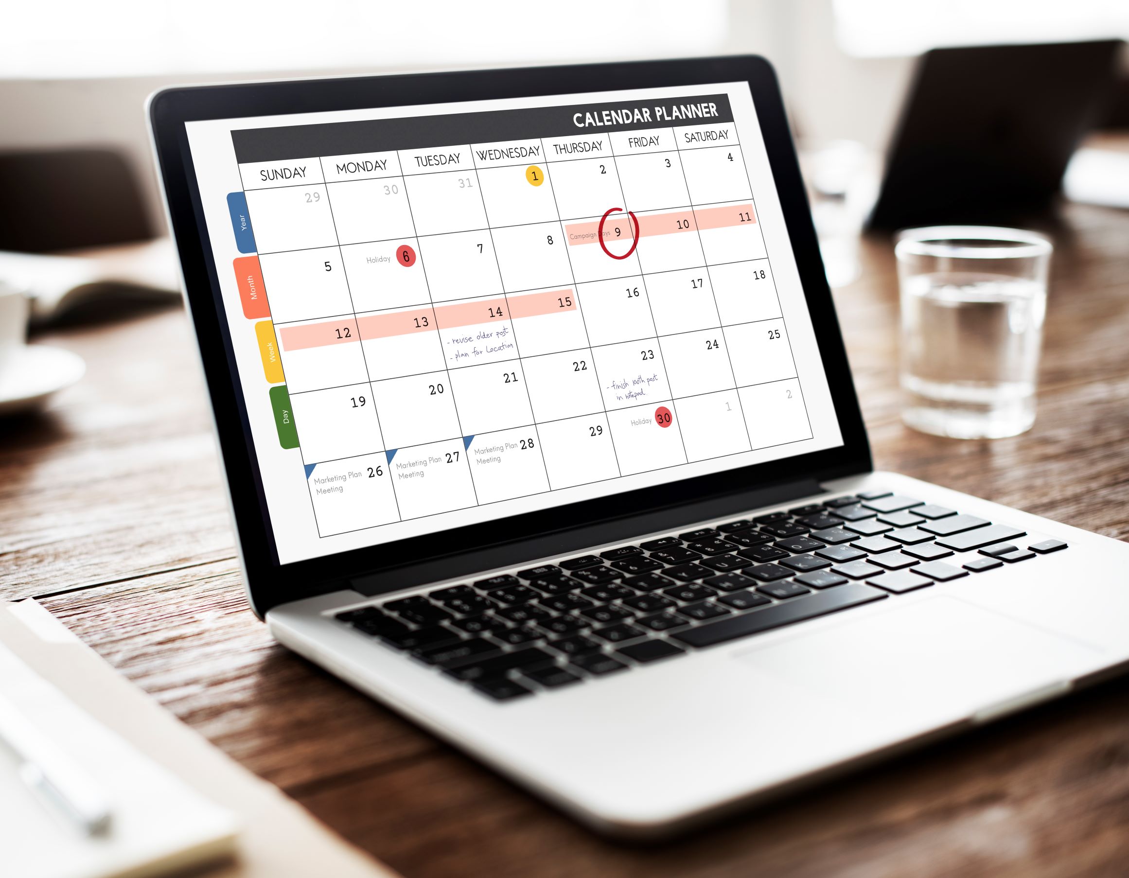 Open laptop sitting on a desk. On the screen is a calendar with entries. The date of the 9th is circled in red.