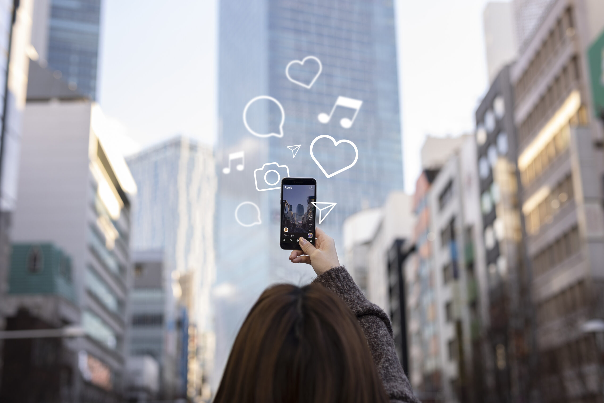 a person taking a picture of a skyscraper with her cellphone and social media icons illustrated around her.