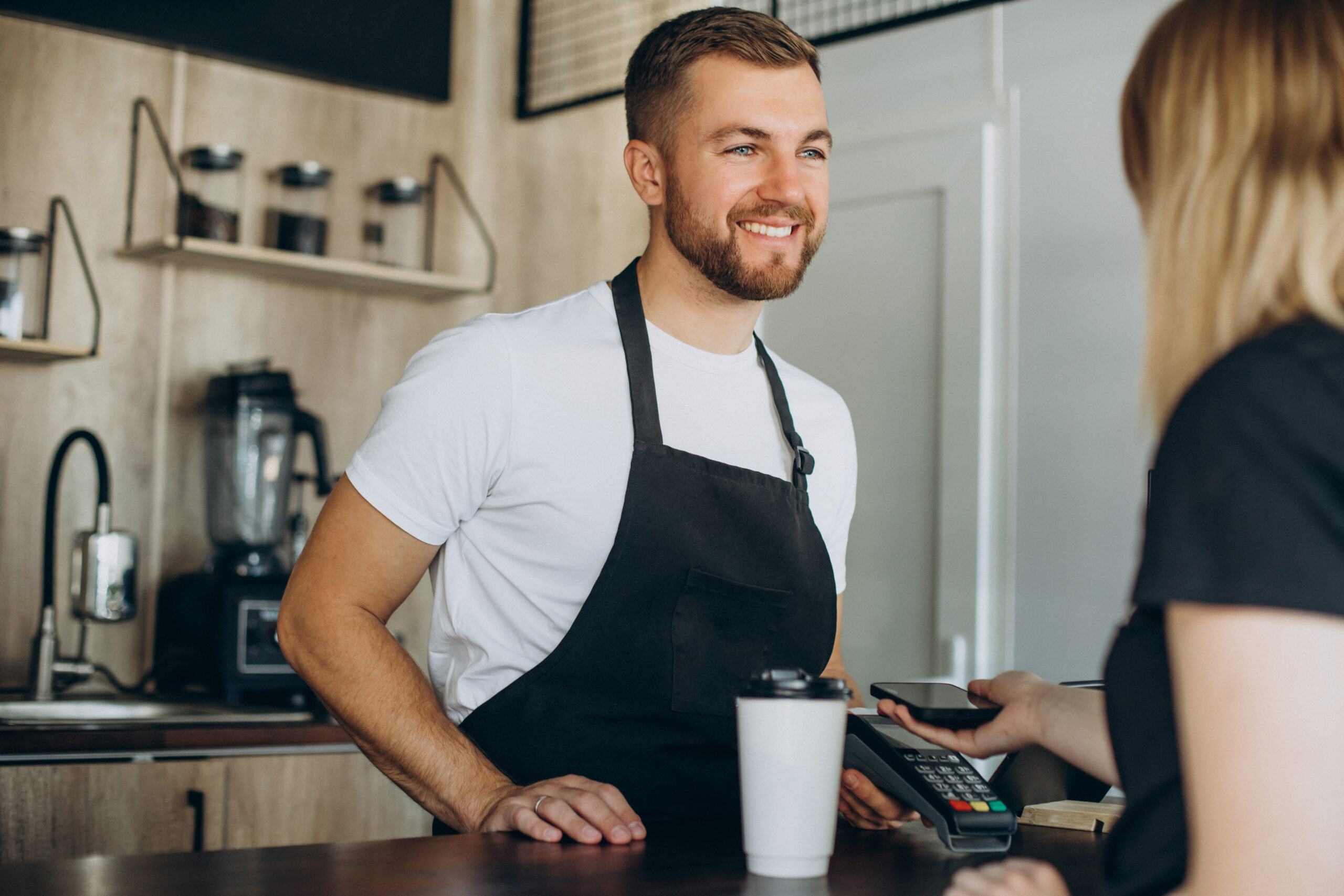 A barista in a coffee shop smiling at a customer with a cup of on the counter