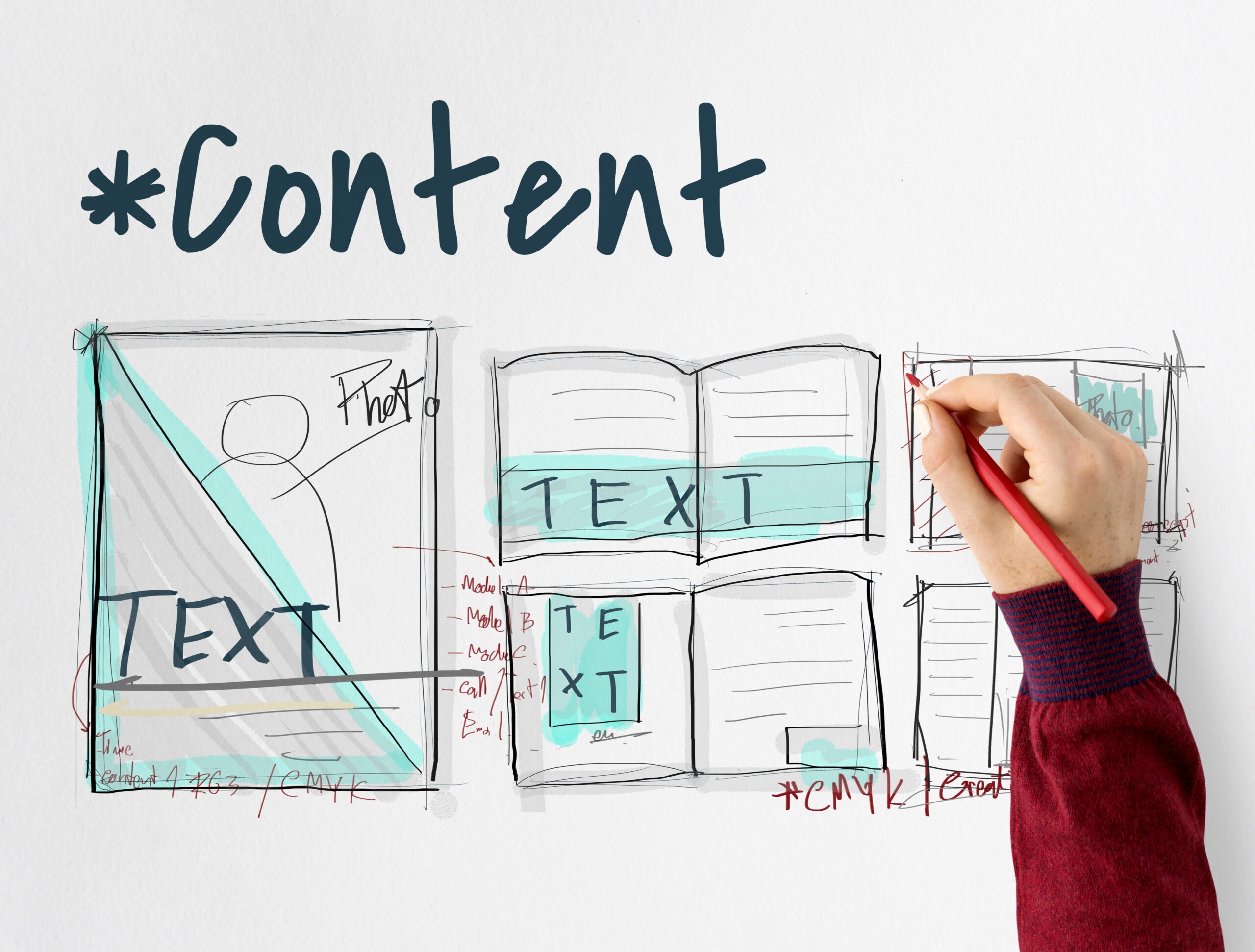 A hand with a red pen writing on an oversized graphic of a website template with the words "content marketing" on top.