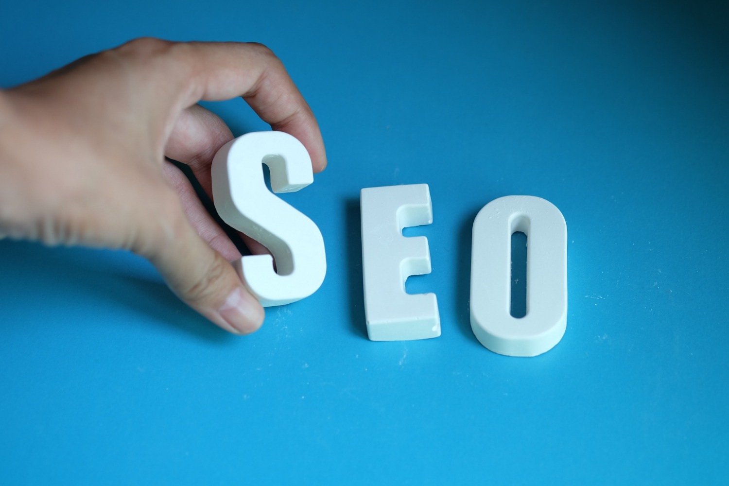 white letters spelling out "SEO" with the S being placed by a hand.