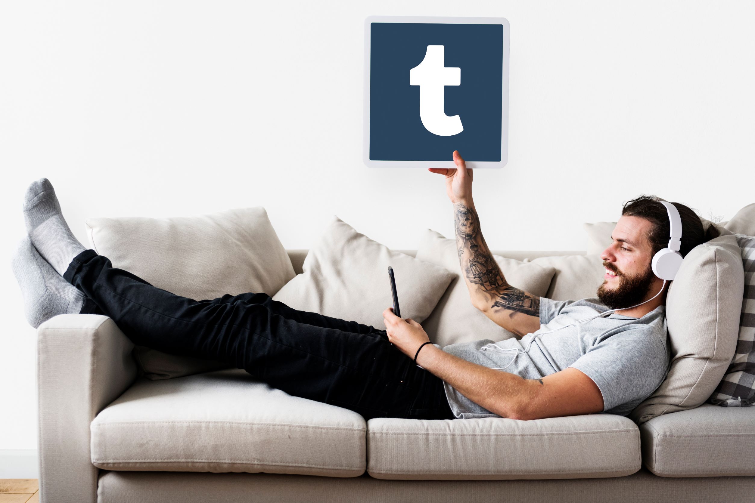 Relaxed hipster man laying on couch, holding up the Tumblr logo