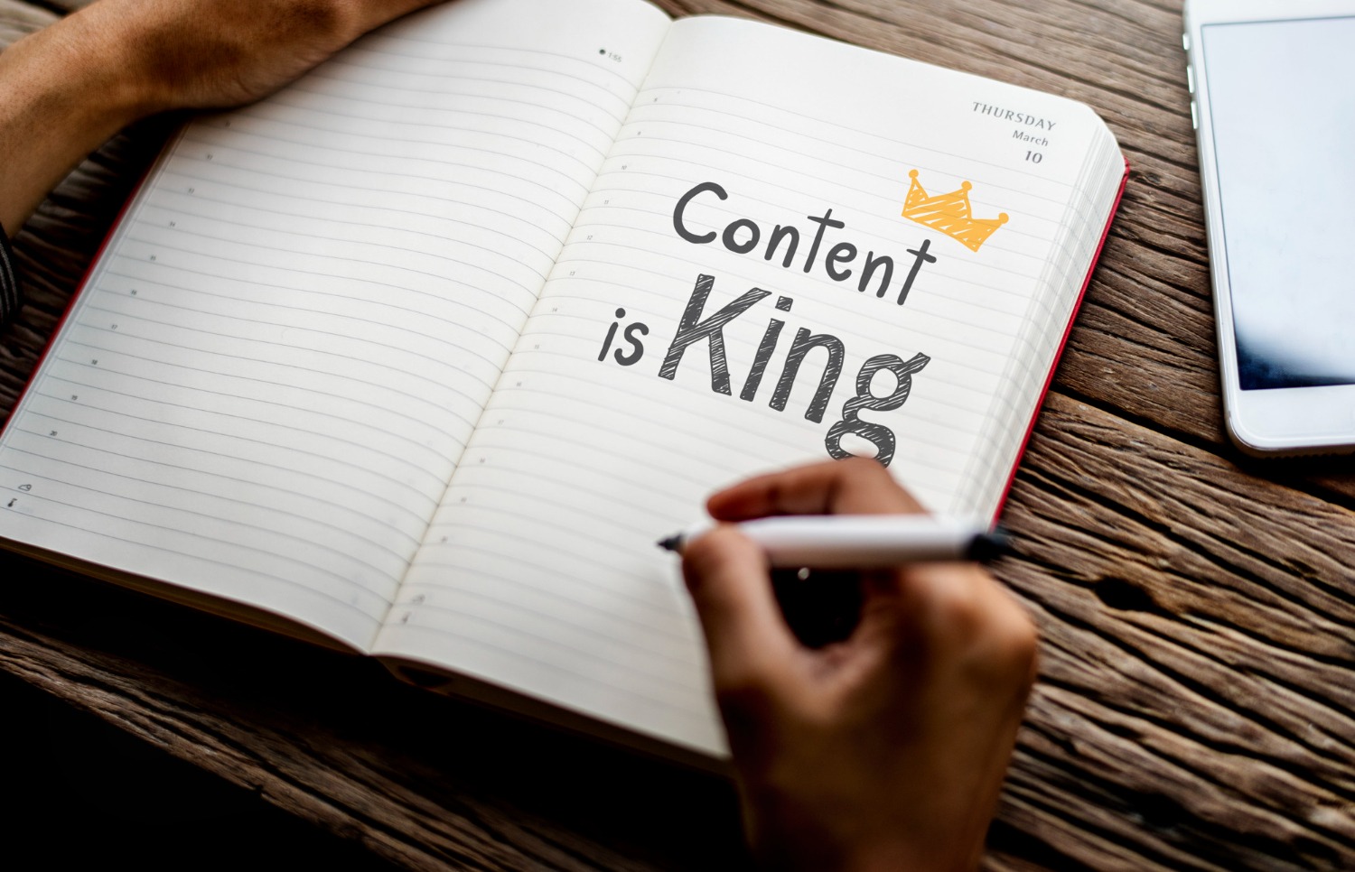 A note with someone's hand holding it while they write the words "Content Is King" in black while making an illustration of a crown on top of it.